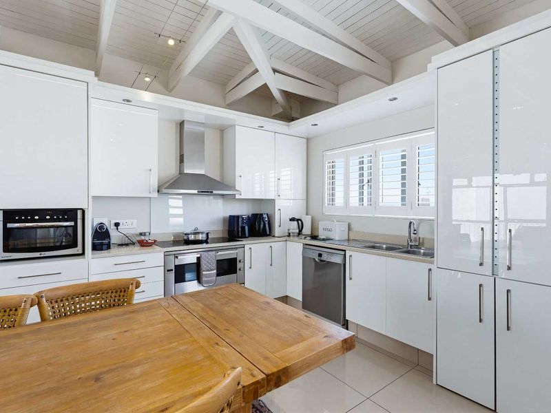 Modern kitchen featuring white gloss cabinetry, stainless steel appliances, tiled flooring, and a striking exposed timber beam ceiling with plantation shutters.