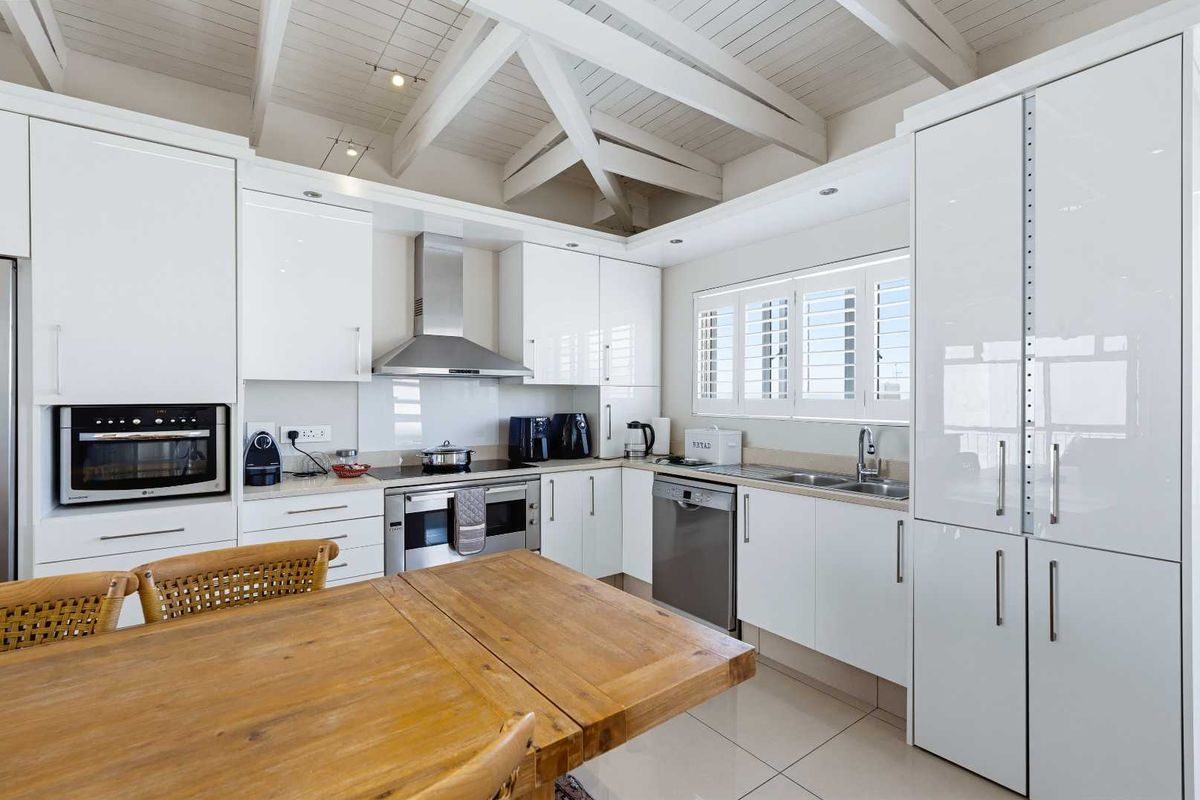 Modern kitchen featuring white gloss cabinetry, stainless steel appliances, tiled flooring, and a striking exposed timber beam ceiling with plantation shutters.