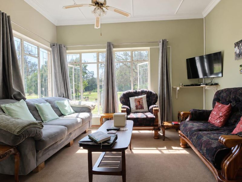 A sunlit living room featuring large windows with garden views, neutral wall tones, and a ceiling fan.