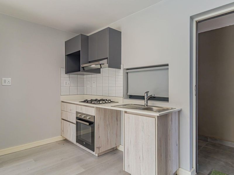 A modern, compact kitchen featuring light wood-look cabinetry, a gas hob, built-in oven, extractor fan, and a stainless steel sink with a tiled splashback.