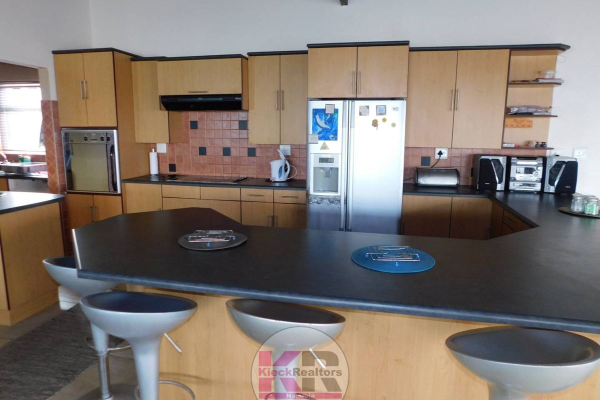 A functional kitchen featuring light wood cabinetry, dark countertops, a breakfast bar, and built-in oven with extractor fan.
