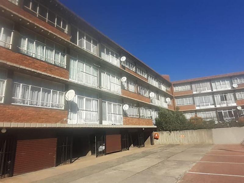 Exterior view of a multi-story apartment complex featuring a brick facade, private balconies, and a paved ground-level parking area.