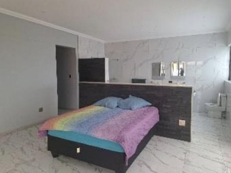 Spacious bedroom featuring an open-plan en-suite bathroom with marble-look tiling, a central partition wall, and integrated vanity area.