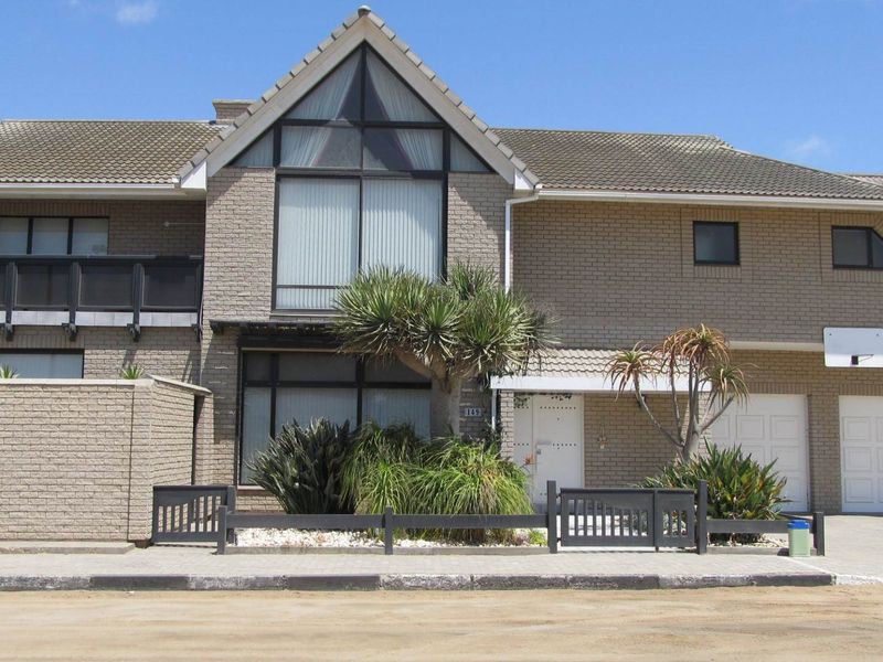 Front elevation of a double-story brick house featuring a tiled roof, balcony, and integrated double garage with a paved driveway.