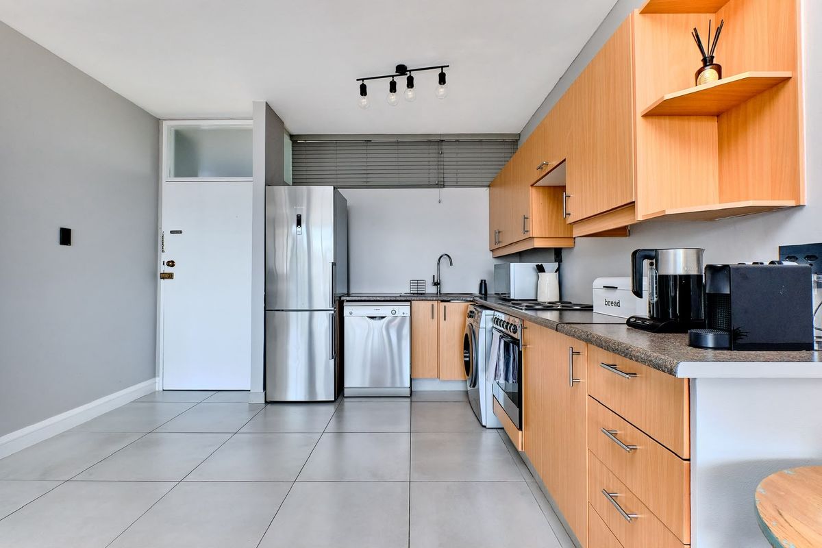 A functional kitchen featuring light wood cabinetry, laminate countertops, tiled flooring, and integrated appliances, offering a clean and practical workspace.