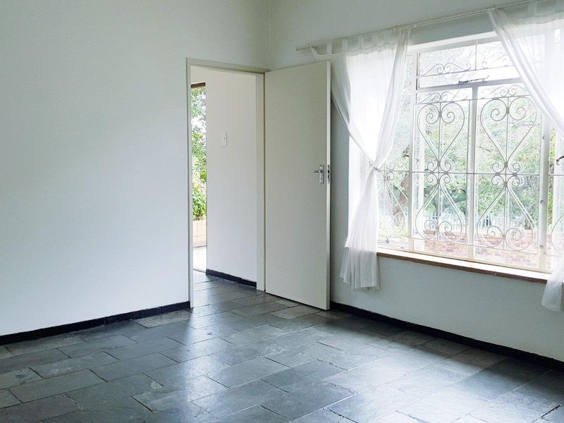 A bright, empty bedroom featuring durable slate tile flooring and a large window with decorative wrought iron security bars.