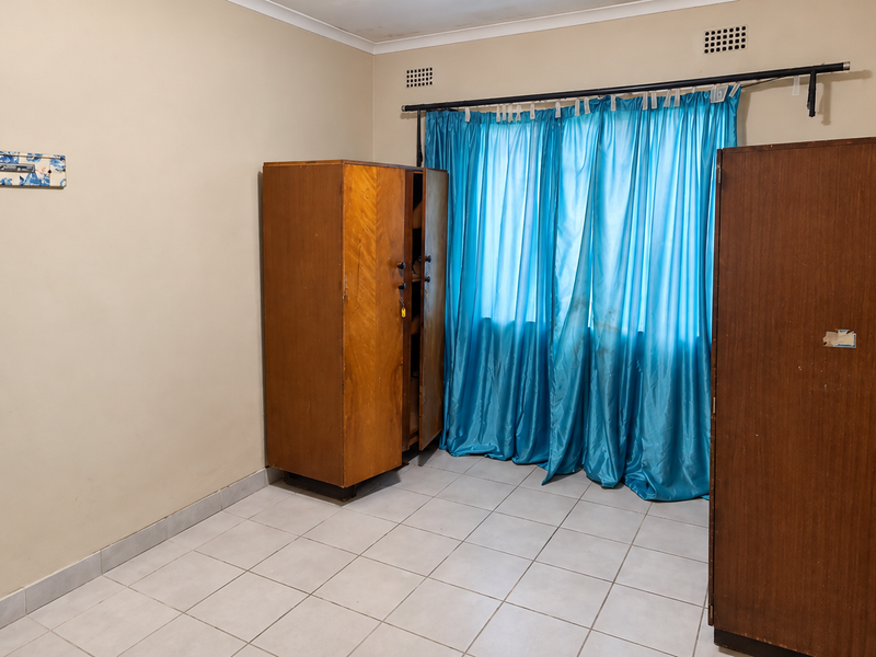 A bedroom featuring tiled flooring, neutral wall finishes, and ventilation grilles, providing a functional space ready for modernization.