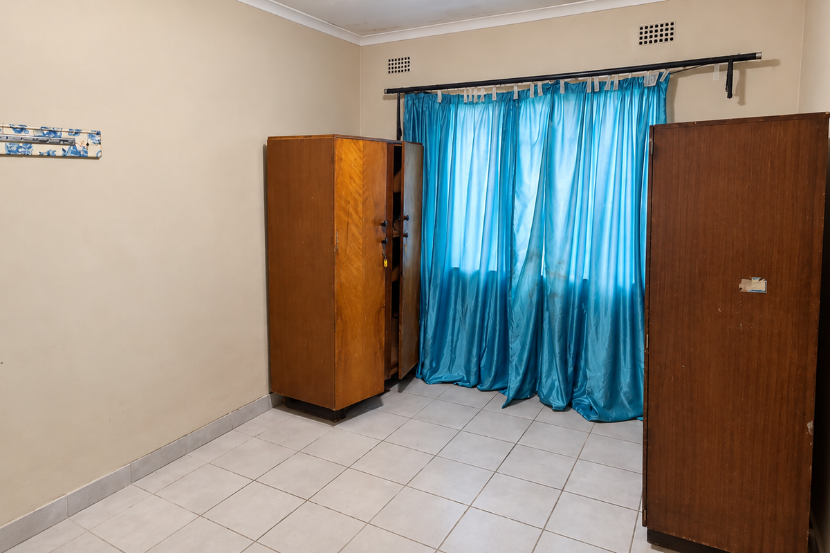 A bedroom featuring tiled flooring, neutral wall finishes, and ventilation grilles, providing a functional space ready for modernization.
