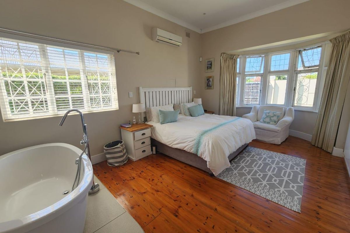 Spacious bedroom featuring polished timber flooring, a freestanding bathtub, split-system air conditioning, and large windows providing ample natural light.