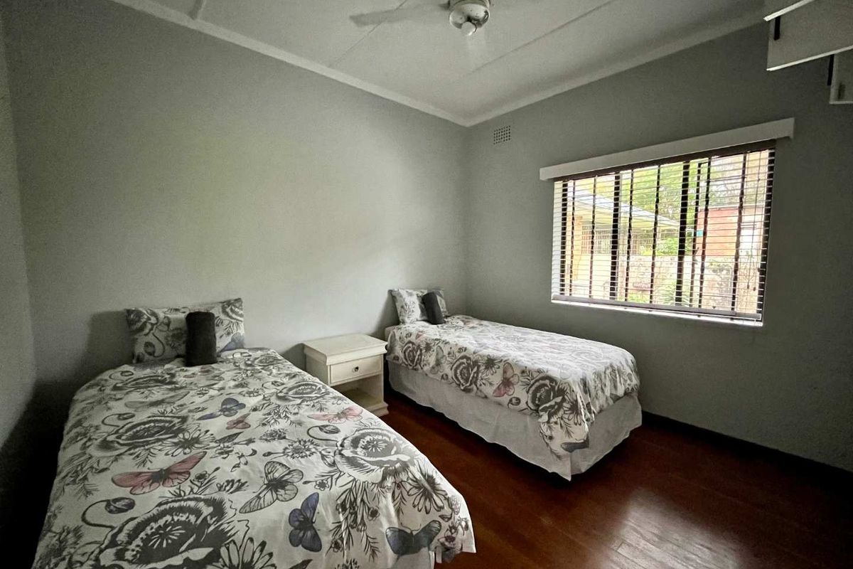 A well-lit bedroom featuring polished wooden flooring, a ceiling fan, and venetian blinds, offering a comfortable and functional living space.