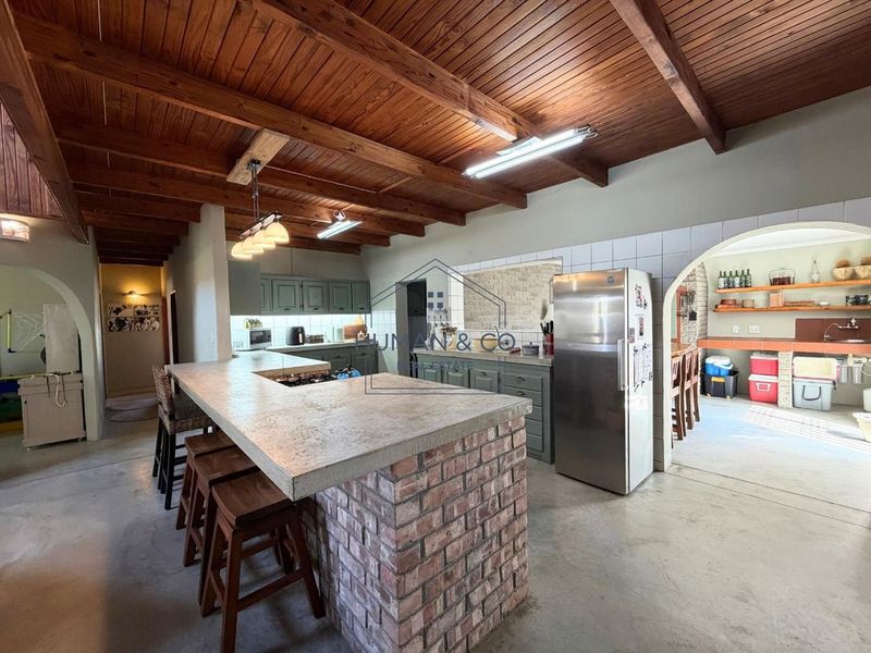 Open plan kitchen featuring a brick island with concrete countertop, exposed timber ceiling beams, and an adjacent scullery area.