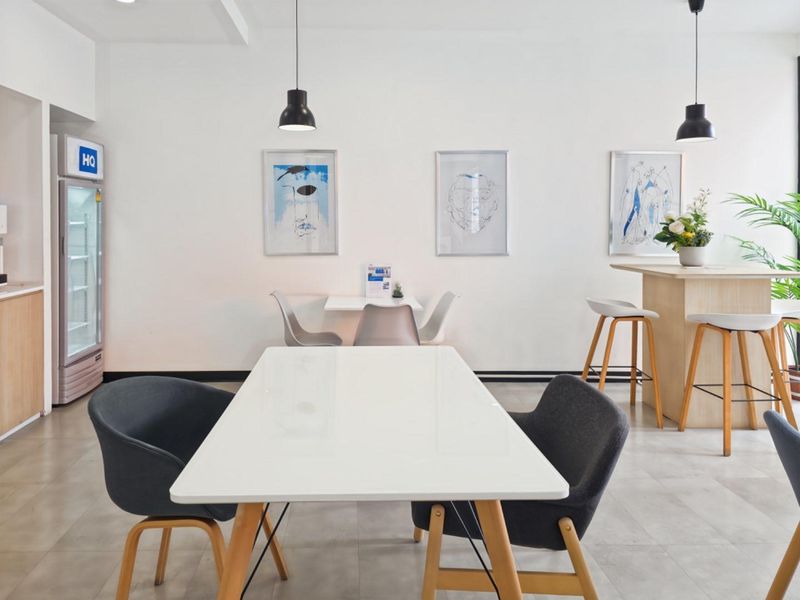 A bright, modern office break-out area featuring tiled flooring, pendant lighting, and a functional kitchenette area with built-in cabinetry.