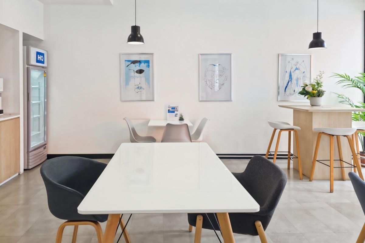 A bright, modern office break-out area featuring tiled flooring, pendant lighting, and a functional kitchenette area with built-in cabinetry.
