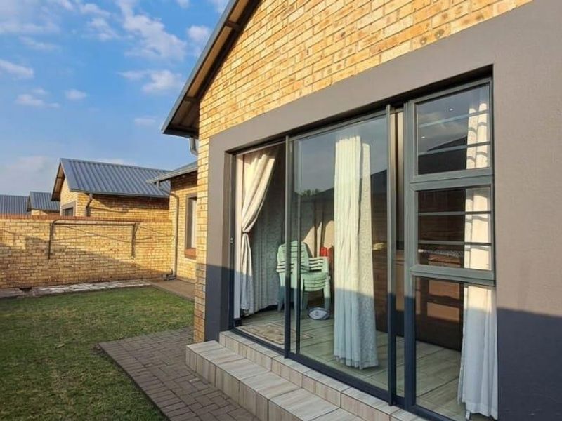 Rear view of the cluster home featuring a face brick facade, sliding glass doors leading to a paved patio, and a private garden area.