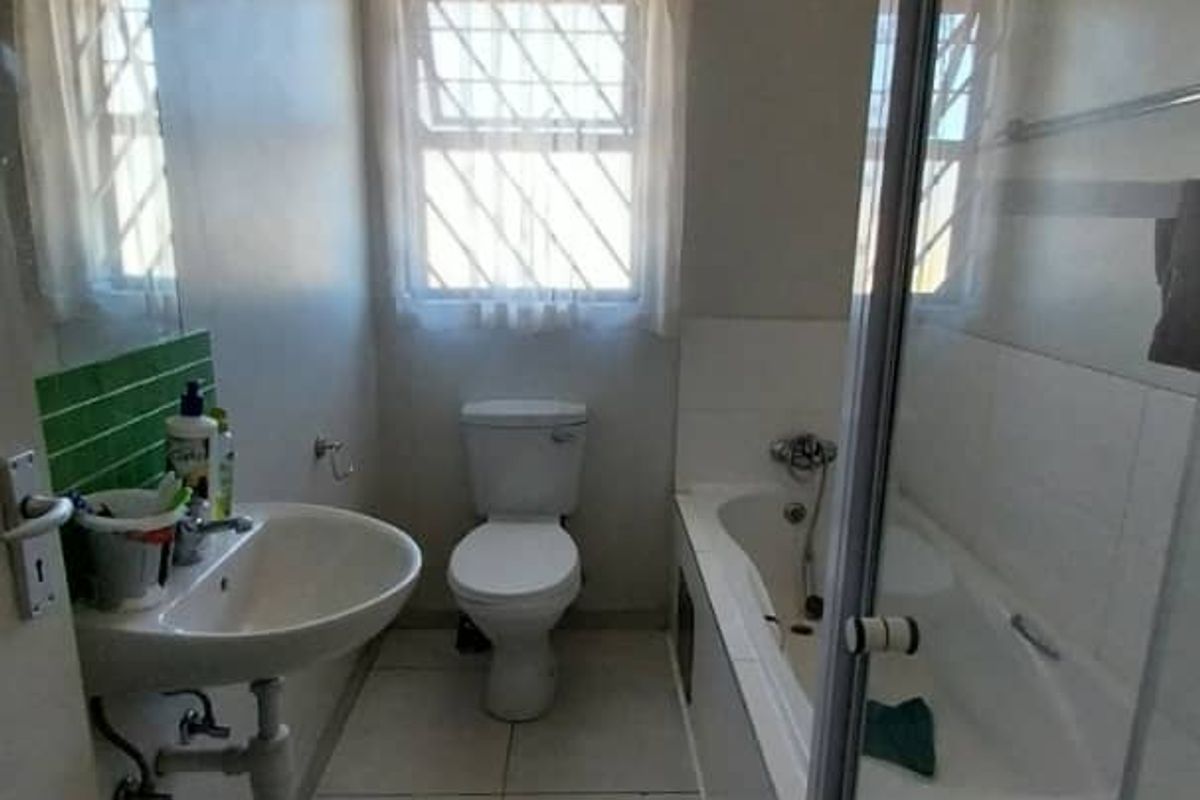 A functional bathroom featuring a wall-mounted basin, a standard toilet, and a combined bathtub and shower enclosure with tiled flooring.