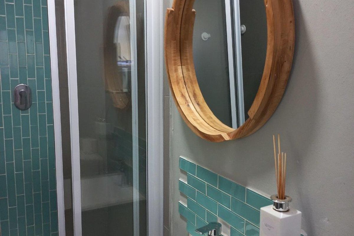 Modern bathroom featuring a vanity with a basin, teal subway tile backsplash, and a glass-enclosed shower.