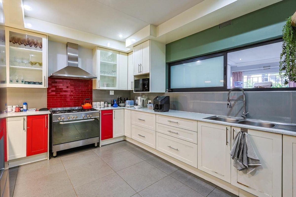 A well-appointed kitchen featuring cream cabinetry, a red tiled splashback, stainless steel gas stove with extractor fan, and a double basin sink.