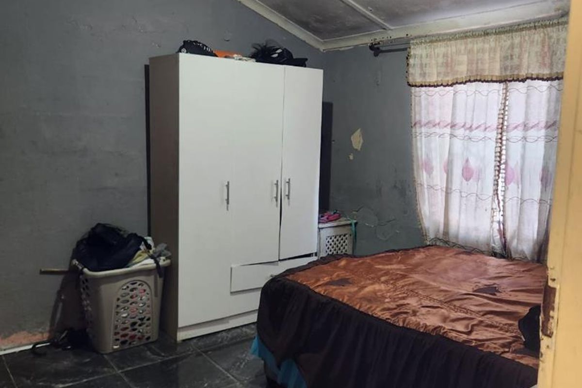 A bedroom featuring dark tiled flooring and grey walls, currently showing signs of wear including peeling paint and damaged ceiling finishes.