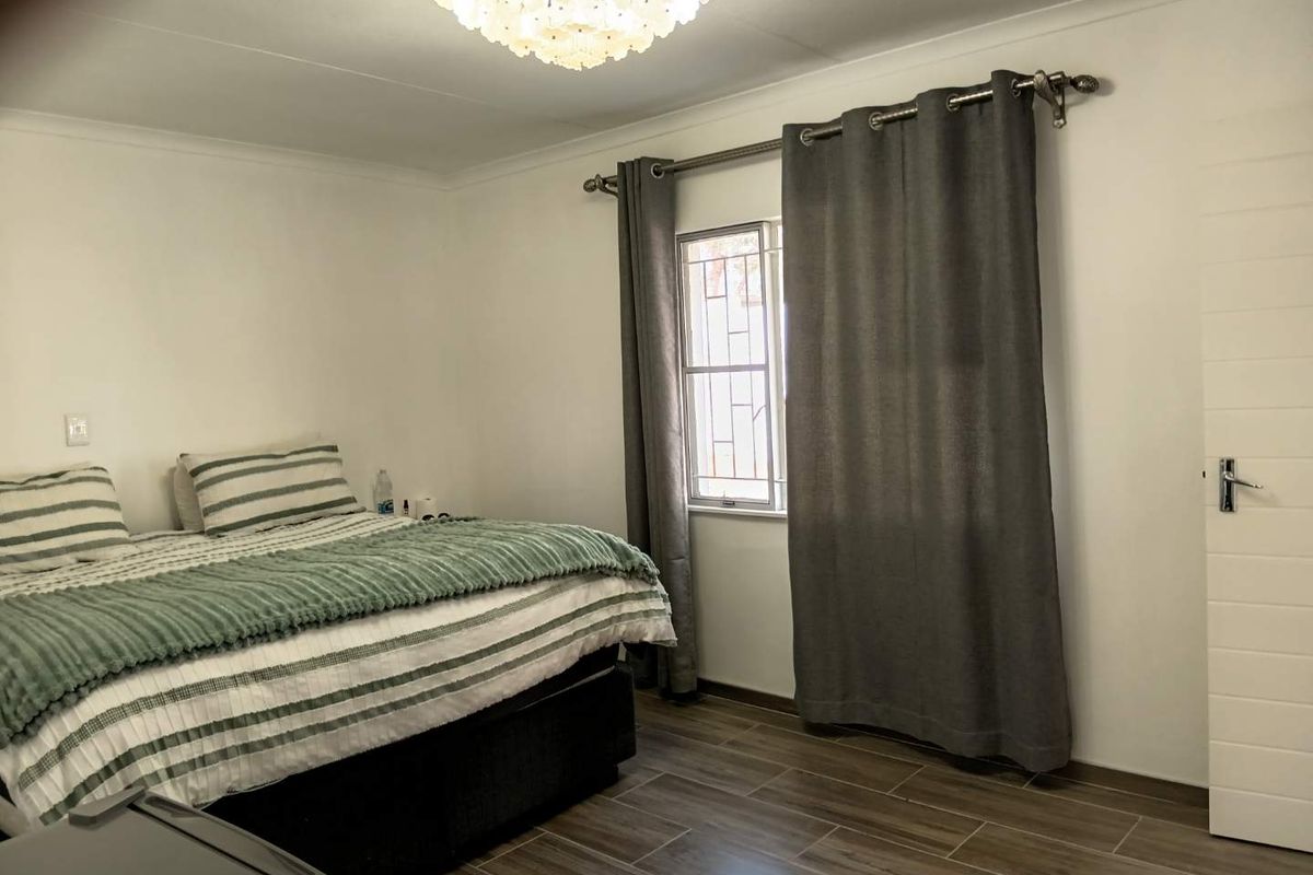 A well-maintained bedroom featuring tiled flooring, a window with security bars, and a central ceiling light fixture.