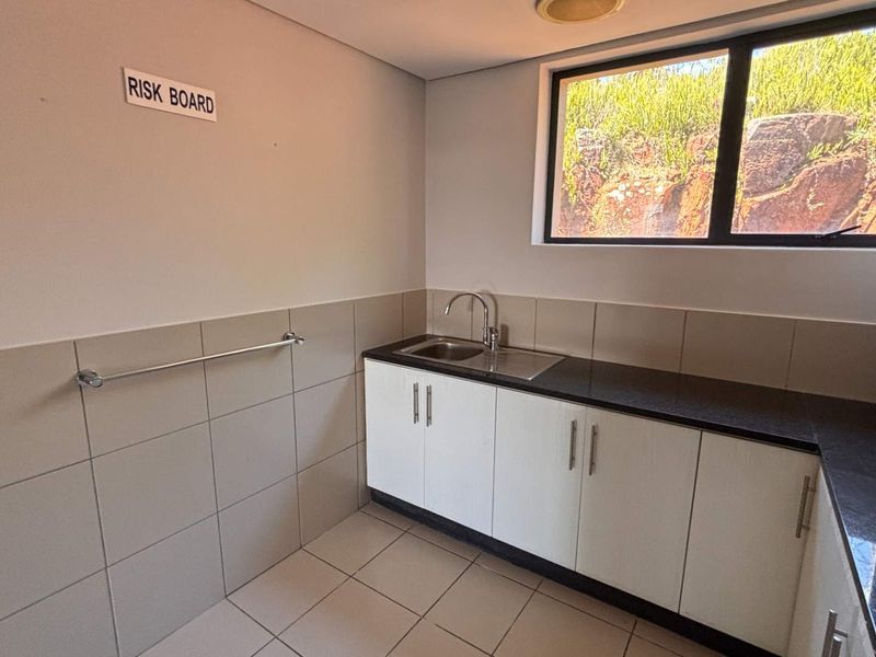 A clean and functional kitchenette area featuring built-in cabinetry, granite countertops, a stainless steel sink, and tiled finishes.