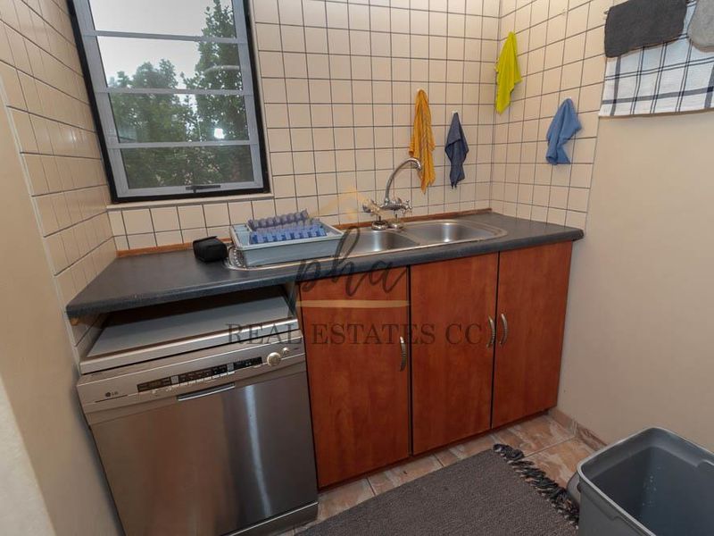 A functional laundry area featuring a double basin sink, laminate countertop, tiled splashback, and built-in cabinetry with space for a dishwasher.