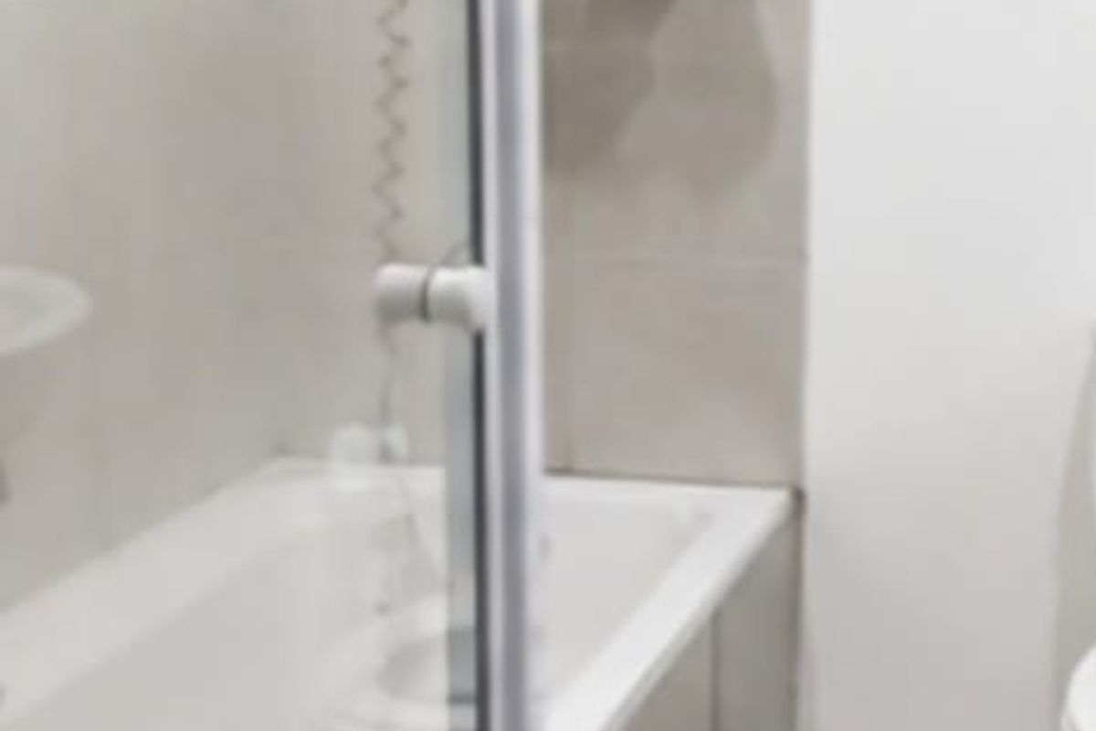 A functional bathroom featuring a bathtub with a glass shower screen, tiled walls, and standard sanitary fixtures.