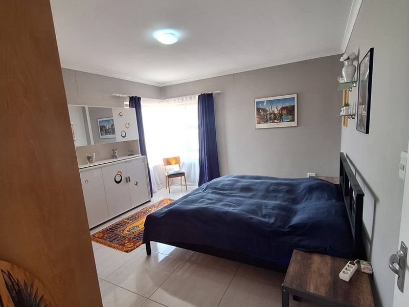 A well-lit bedroom featuring neutral wall tones, large format floor tiles, and classic cove cornicing, offering a clean and functional living space.