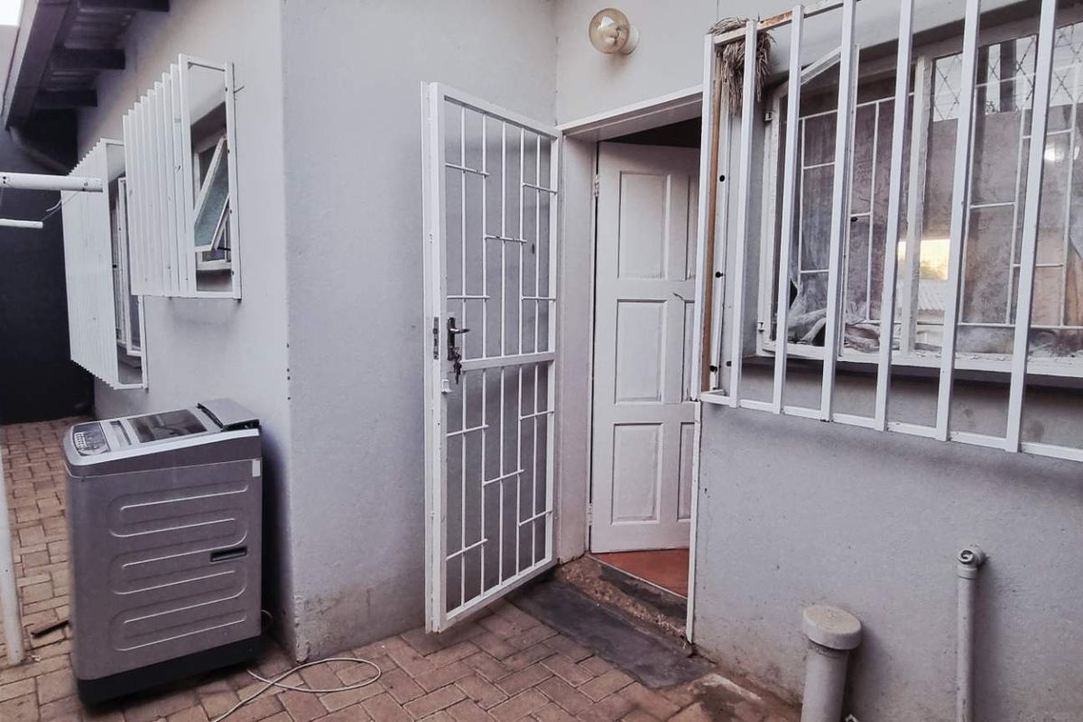 Rear exterior area featuring paved flooring, security gates, and window burglar bars, providing access to the property's rear entrance.