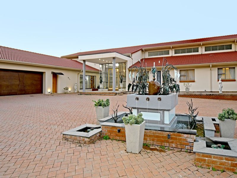 Spacious front exterior featuring a paved driveway, a central water fountain, and a covered entrance portico leading to the main residence.
