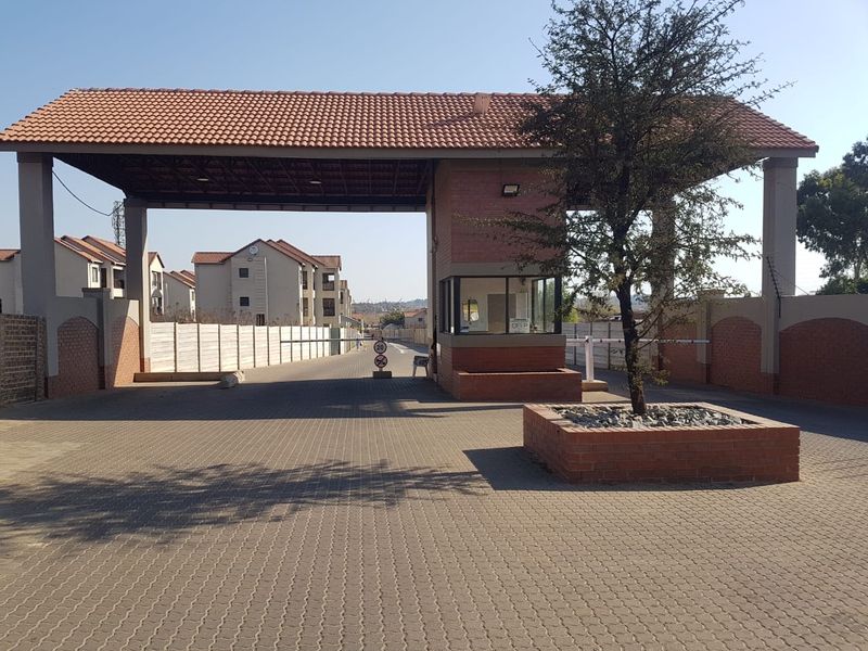 A secure residential complex entrance featuring a brick gatehouse, paved driveway, and controlled boom gate access.