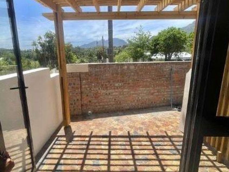Outdoor patio area featuring a wooden pergola, brick boundary wall, and paved flooring, offering scenic mountain views.