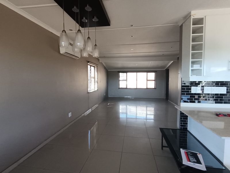 Spacious open-plan living area featuring polished tile flooring, modern pendant lighting, air conditioning, and a contemporary kitchen with stone countertops and subway tile backsplash.