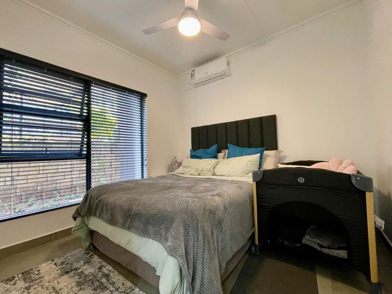 A well-maintained bedroom featuring a ceiling fan, split-system air conditioning, and large windows with venetian blinds, providing a comfortable and functional living space.