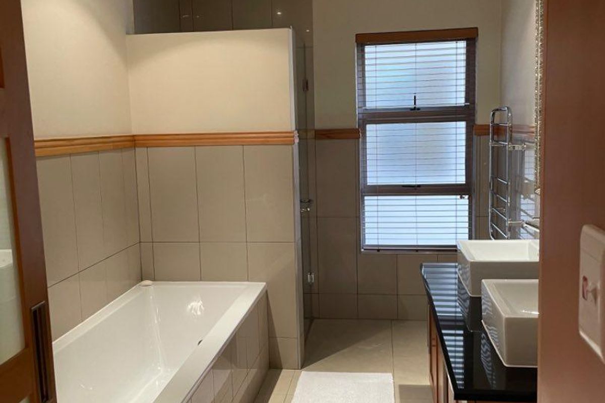 Modern bathroom featuring a tiled bathtub, dual vessel sinks on a dark countertop, wooden vanity cabinetry, and a large window with blinds.