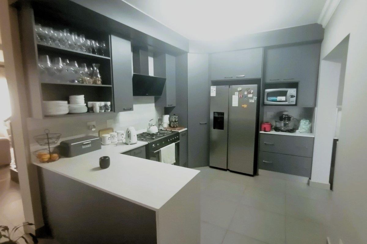 Modern kitchen featuring dark grey cabinetry, stone countertops, a breakfast bar, built-in oven, extractor fan, and integrated microwave space.