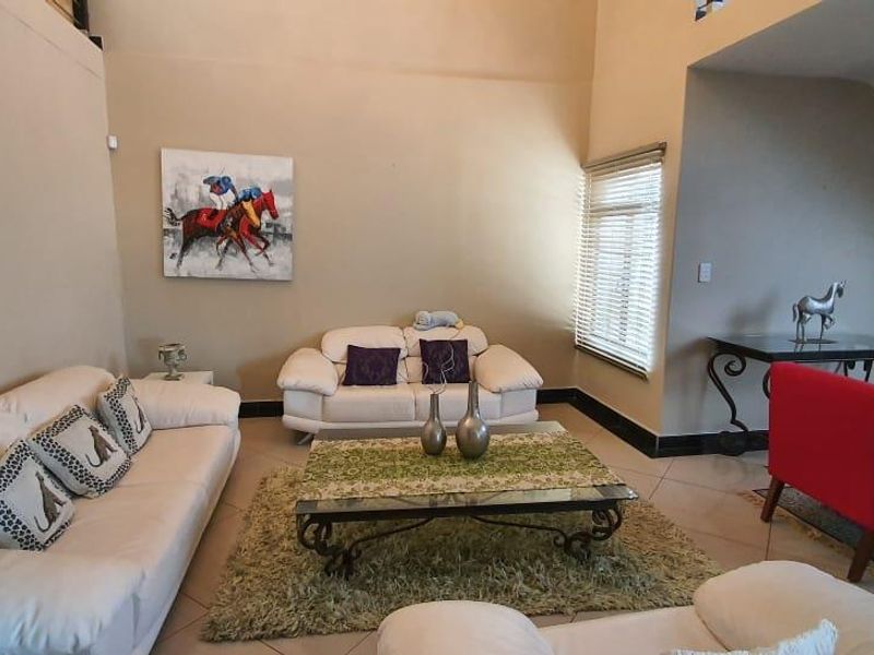 Spacious living room featuring high vaulted ceilings, tiled flooring, and large windows with venetian blinds, offering a bright and open atmosphere.