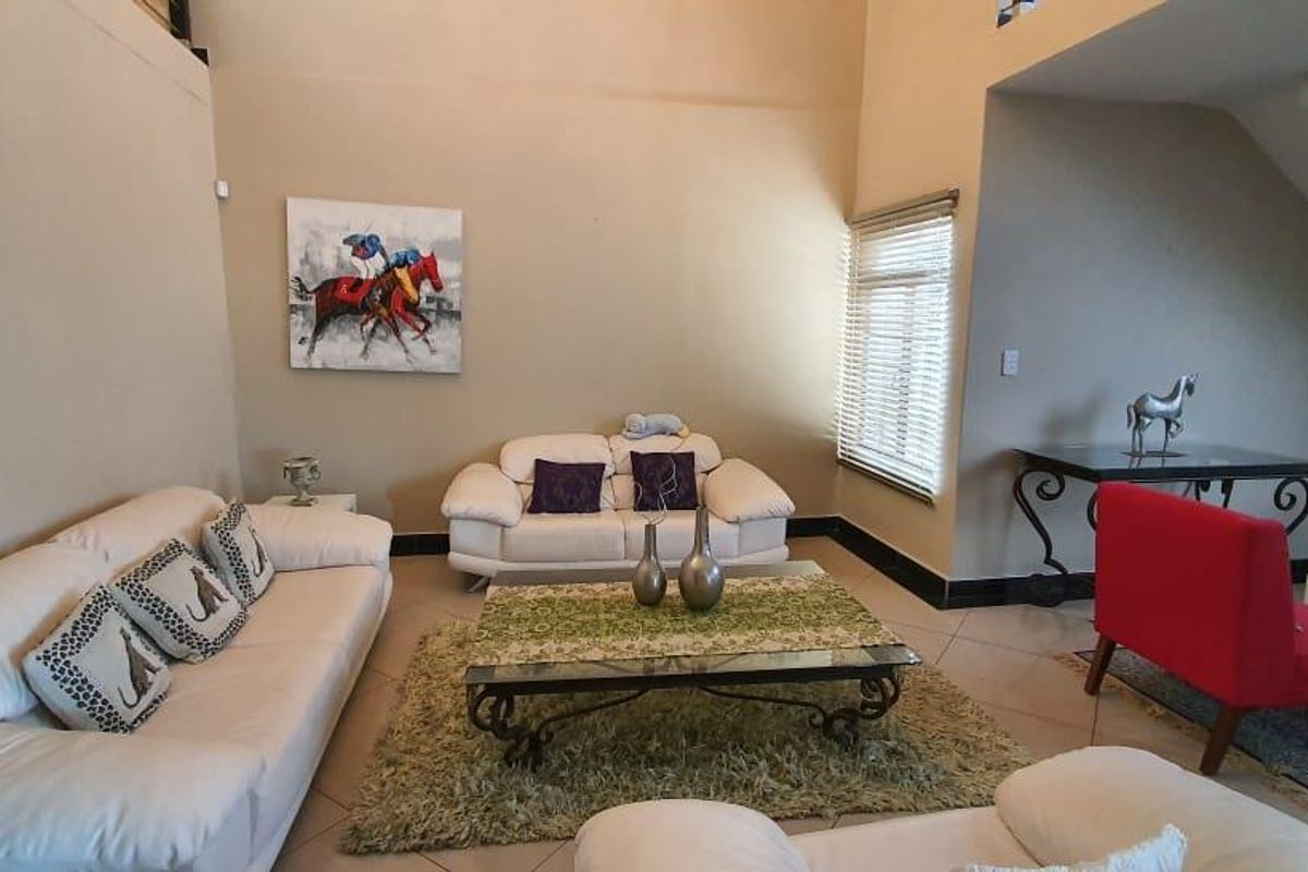 Spacious living room featuring high vaulted ceilings, tiled flooring, and large windows with venetian blinds, offering a bright and open atmosphere.