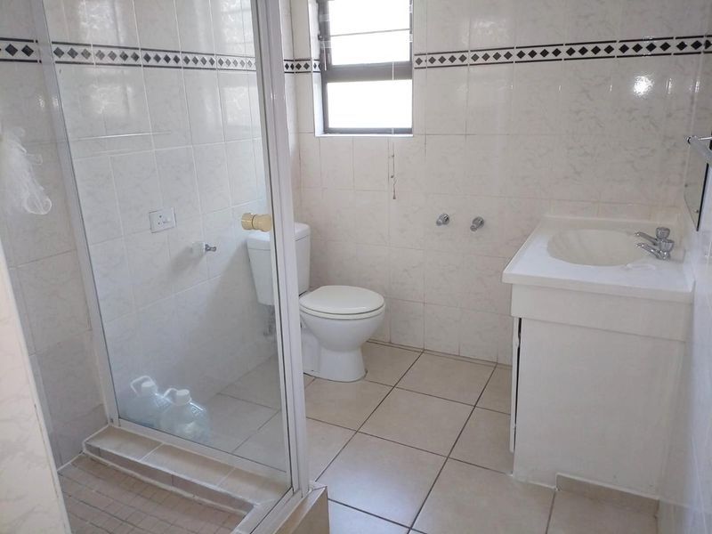 A functional bathroom featuring a glass-enclosed shower, tiled walls and flooring, a vanity basin, and a standard toilet.