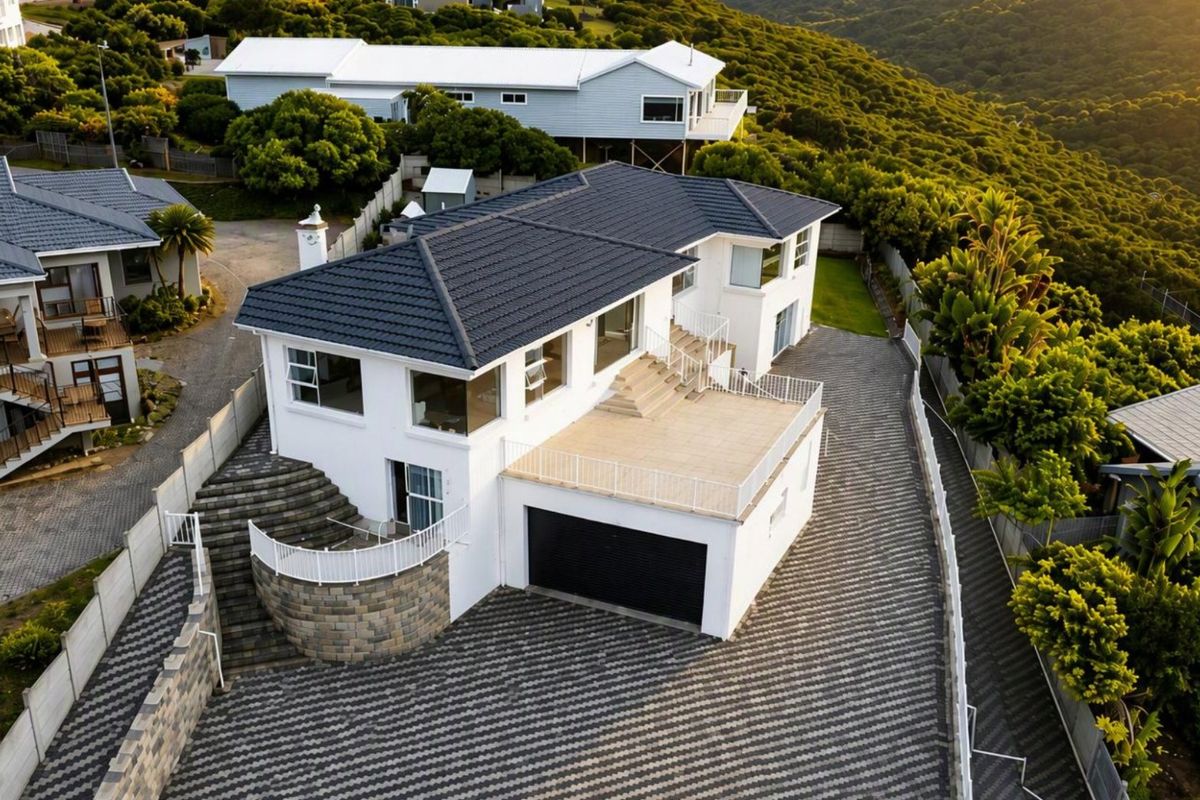 Aerial view of a modern two-story house featuring a tiled roof, paved driveway, double garage, and a spacious raised patio area.