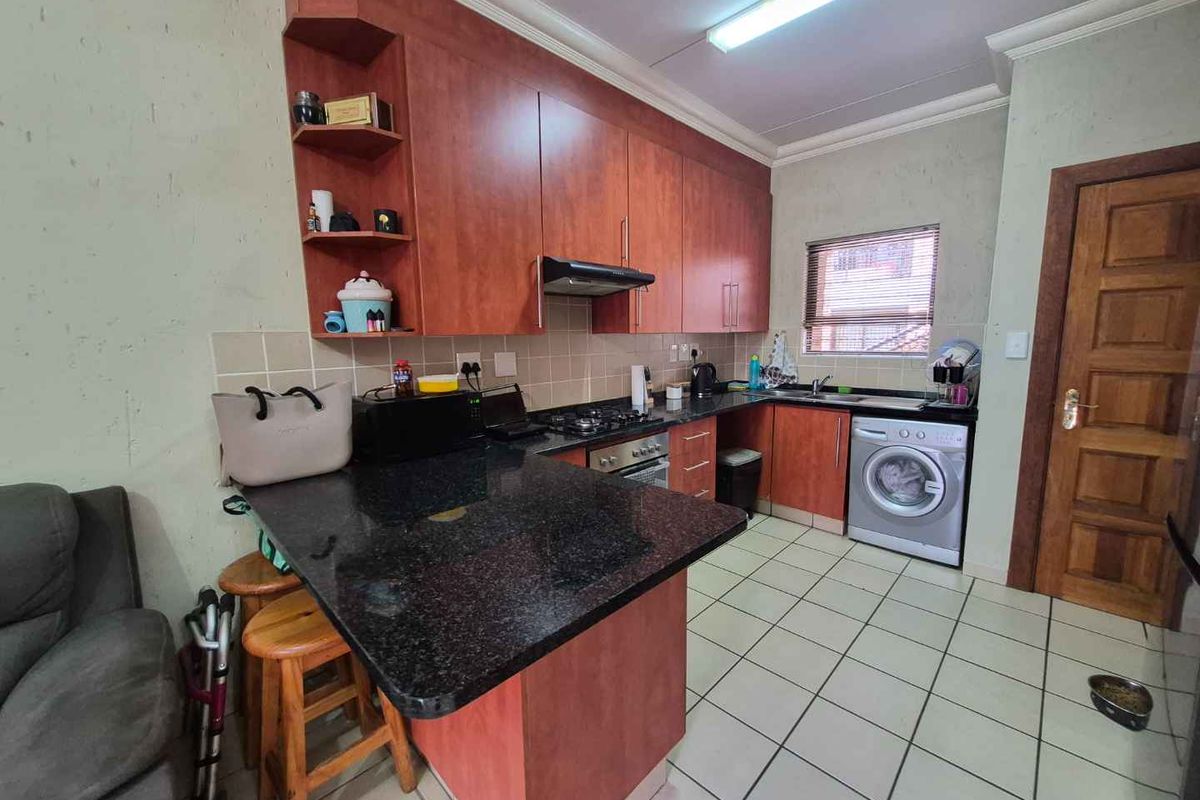 Functional kitchen featuring dark granite countertops, wood-finish cabinetry, built-in gas hob, extractor fan, and integrated laundry appliance space.