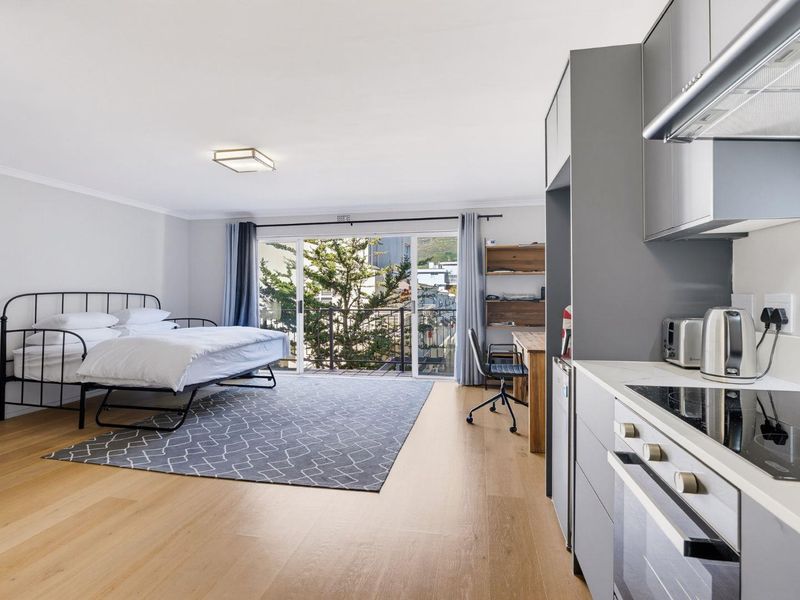 Modern open-plan studio apartment featuring a sleek kitchen with built-in appliances, light wood flooring, and a sliding door leading to a private balcony.
