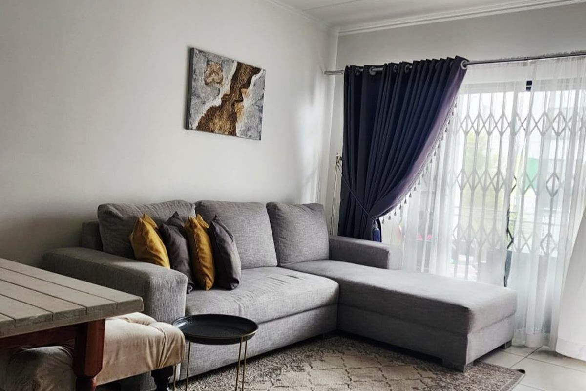 A bright living room featuring tiled flooring, a sliding glass door with security gate, and neutral wall finishes.