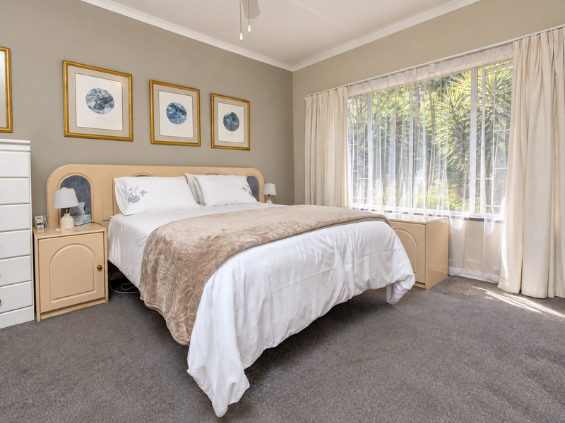A well-maintained bedroom featuring neutral wall tones, carpeted flooring, and built-in headboard and bedside cabinetry, with large windows allowing for natural light.