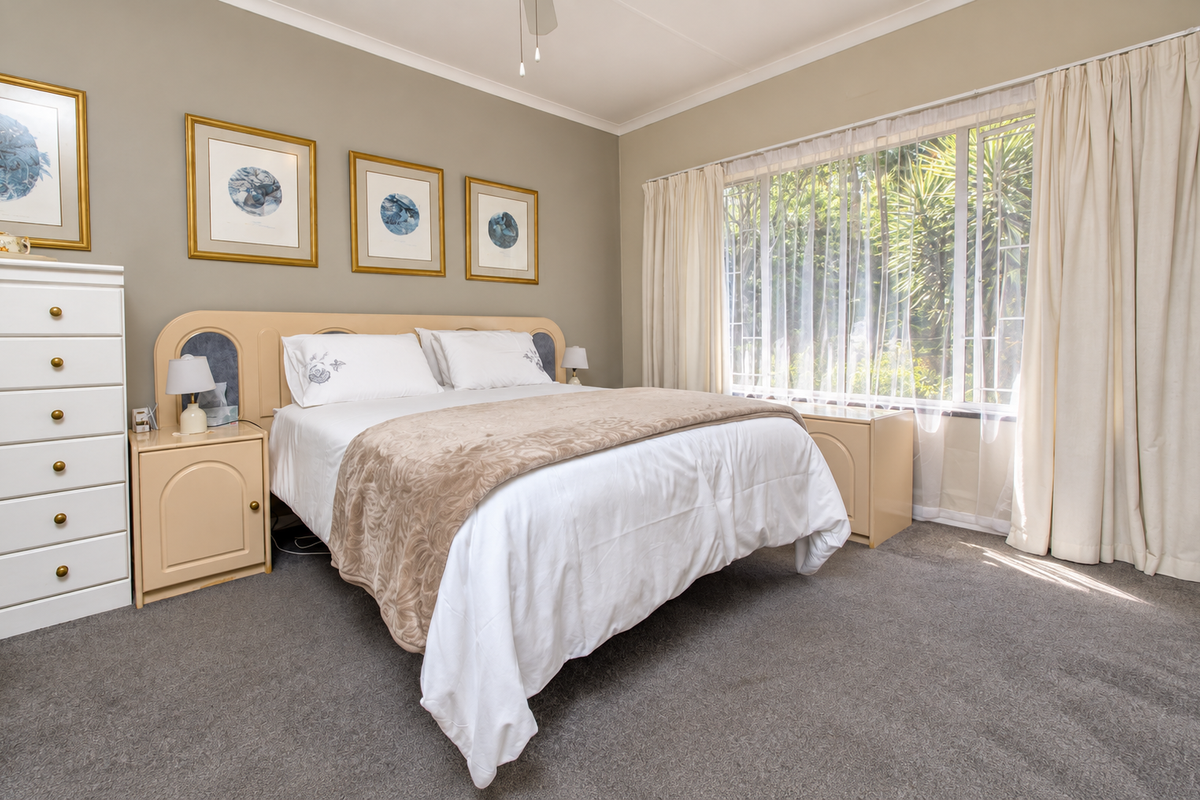 A well-maintained bedroom featuring neutral wall tones, carpeted flooring, and built-in headboard and bedside cabinetry, with large windows allowing for natural light.