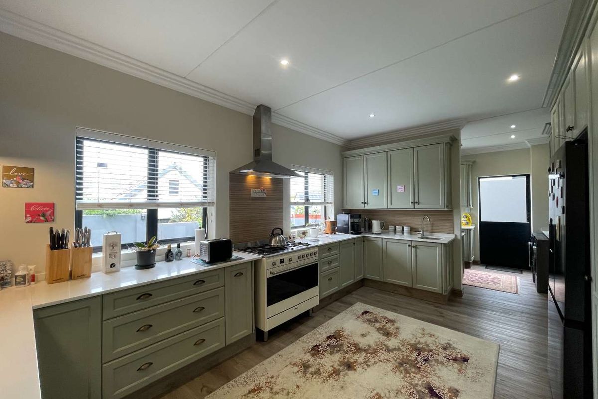 A well-maintained kitchen featuring sage green cabinetry, quartz countertops, a stainless steel extractor fan, and a gas stove with ample natural light.