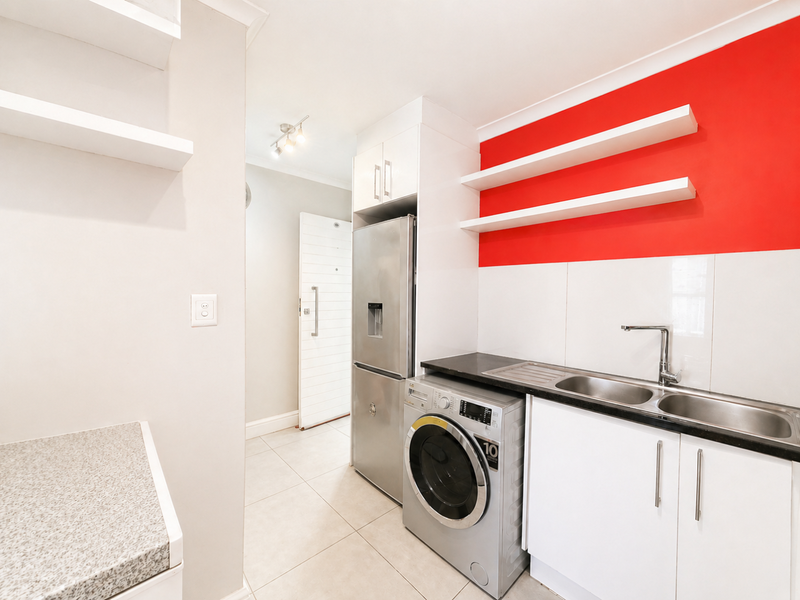 A functional scullery area featuring built-in cabinetry, a stainless steel double sink, floating shelves, and tiled flooring, providing efficient utility space.
