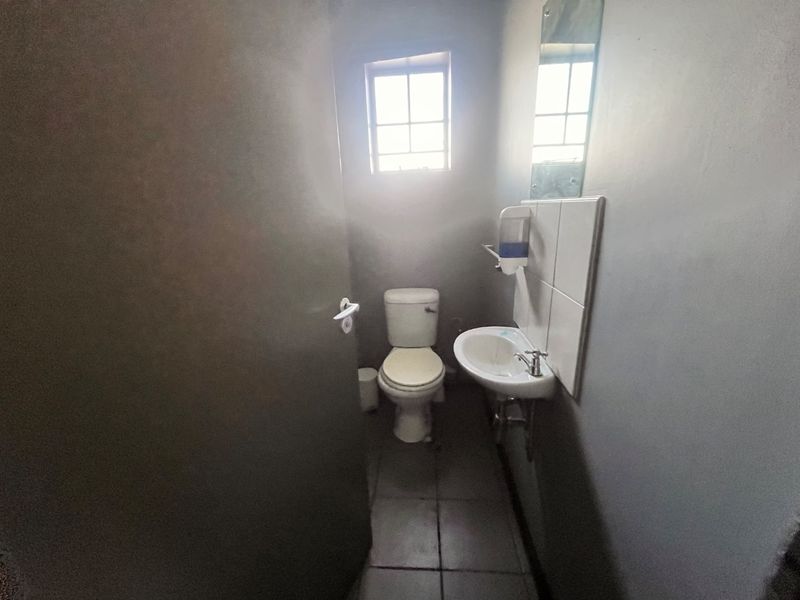 A compact functional bathroom featuring a toilet, wall-mounted basin with tiled splashback, and a mirror.