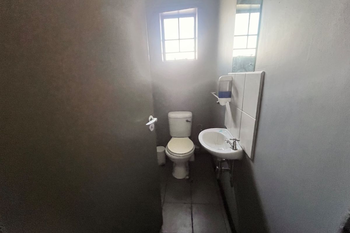 A compact functional bathroom featuring a toilet, wall-mounted basin with tiled splashback, and a mirror.