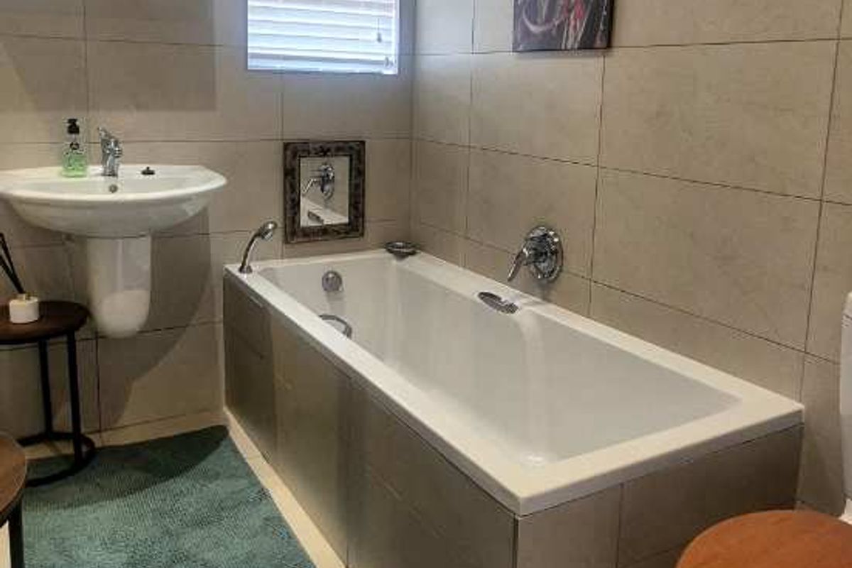 A well-maintained bathroom featuring a pedestal basin, a tiled built-in bathtub, and neutral wall tiling with a decorative mosaic border.