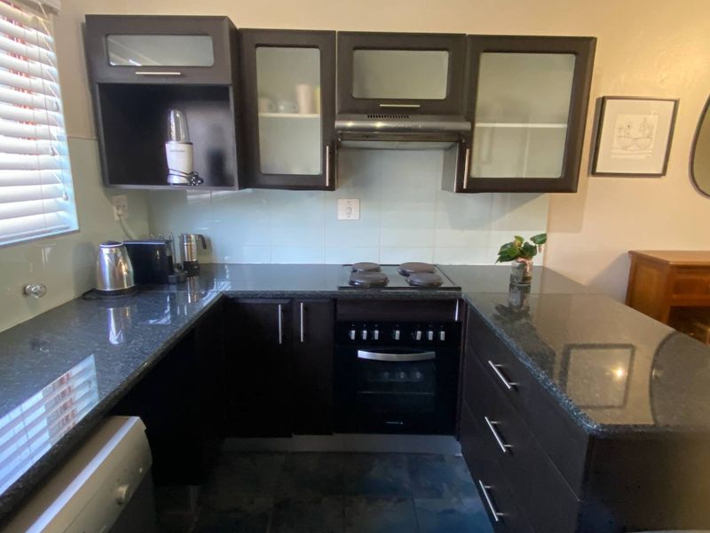 A functional kitchen featuring dark wood cabinetry, granite countertops, built-in oven, electric hob, and extractor fan with a tiled splashback.